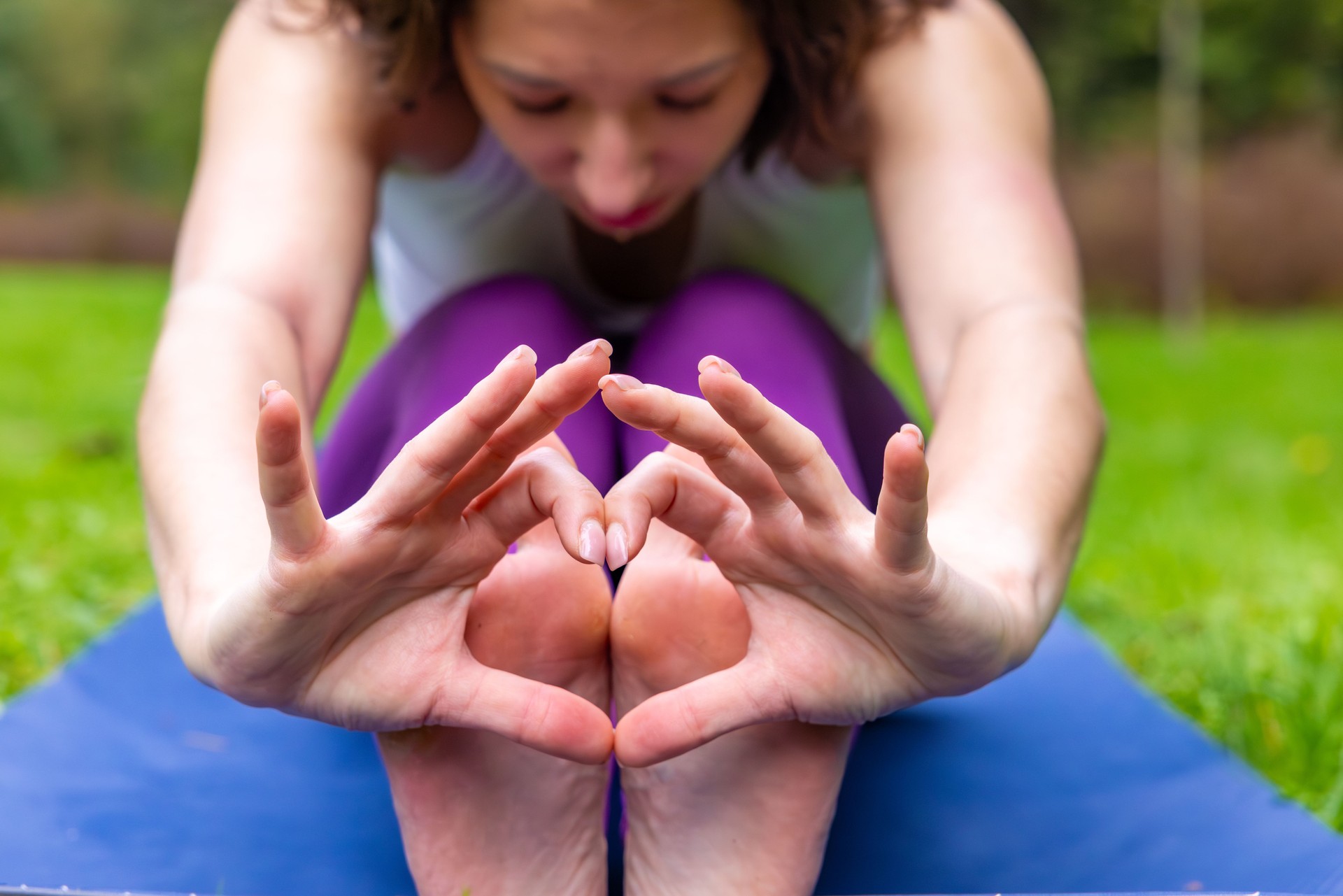 Woman in seated forward fold pose with hands in mudra gesture during outdoor yoga session. Calm and meditative focus